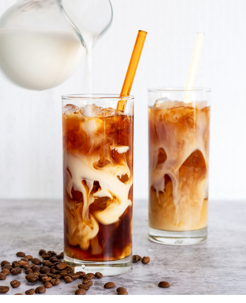 A pitcher of milk being poured into two glasses of iced coffee