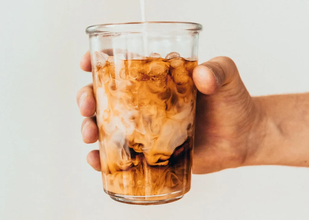 Iced cold glass of cold brew coffee and cream held out in someone's hand