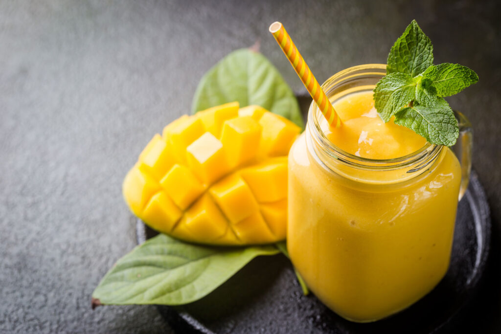 A glass of mango smoothie next to a sliced mango
