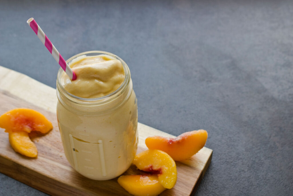 A mason jar filled with a smoothie next to sliced peaches