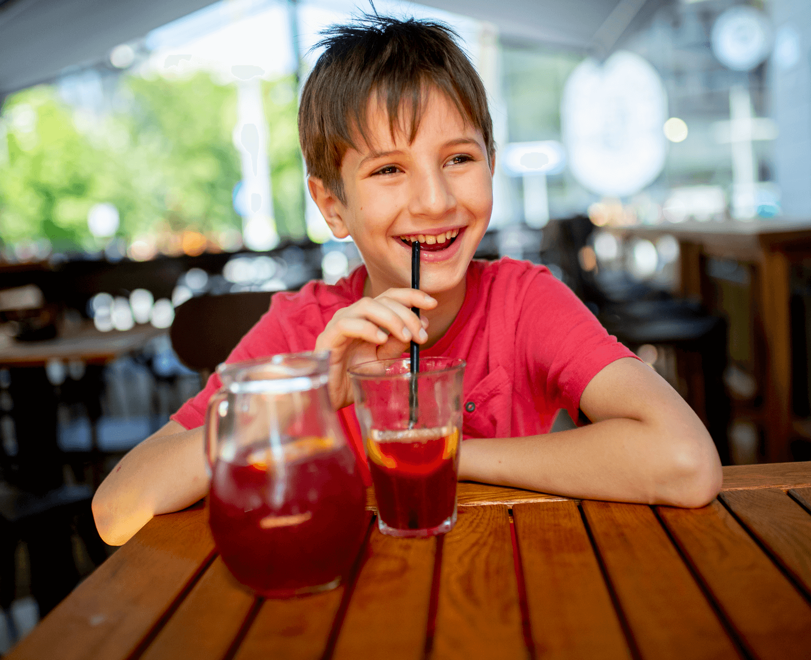 A young boy sitting at a table with two glasses of juice